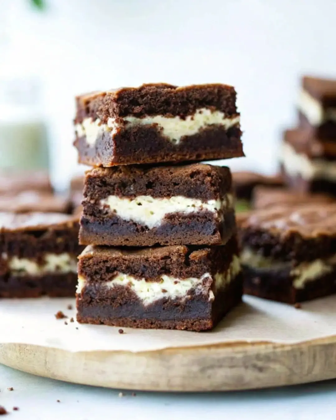 A full tray of freshly baked coconut brownies with a glossy chocolate top, sprinkled desiccated coconut, and powdered sugar, displayed on a white marble surface with tropical leaves.